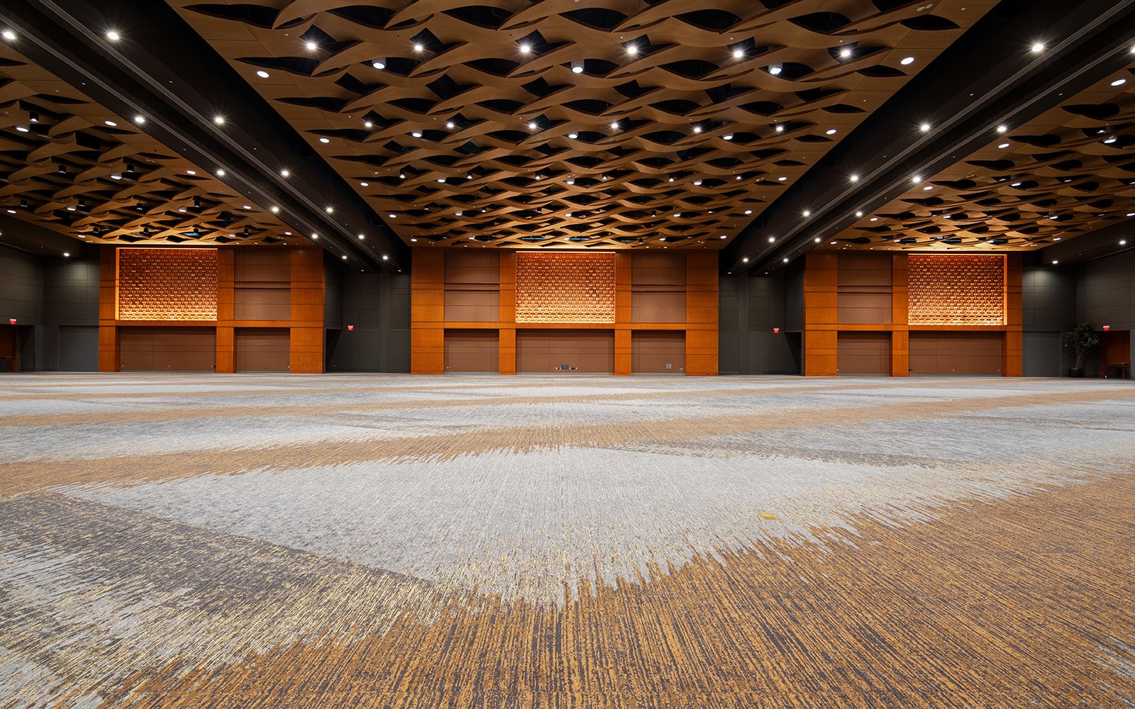 Ground level photo taken of a modern ballroom with warm wood accents, intricate ceiling design, and versatile event lighting.