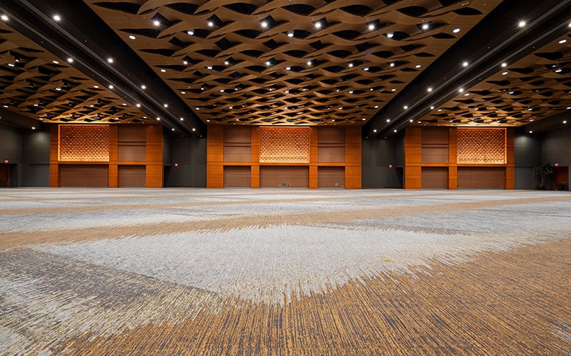 Ground level photo taken of a modern ballroom with warm wood accents, intricate ceiling design, and versatile event lighting.