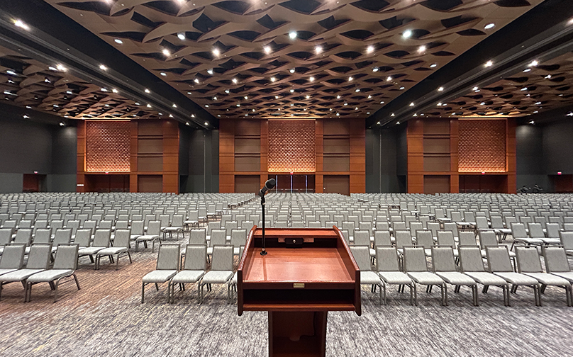 View from the stage of a large ballroom set up in theater style with rows of chairs and a podium.