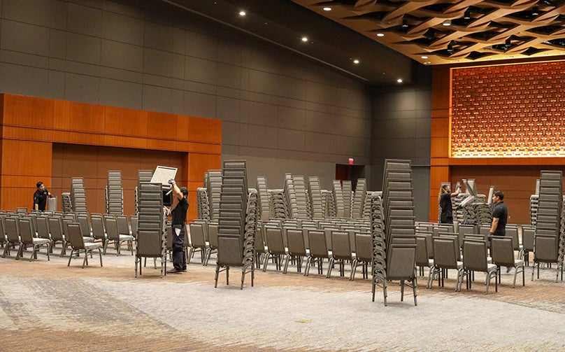 A photo of four employees setting up gray chairs for an event in a ballroom