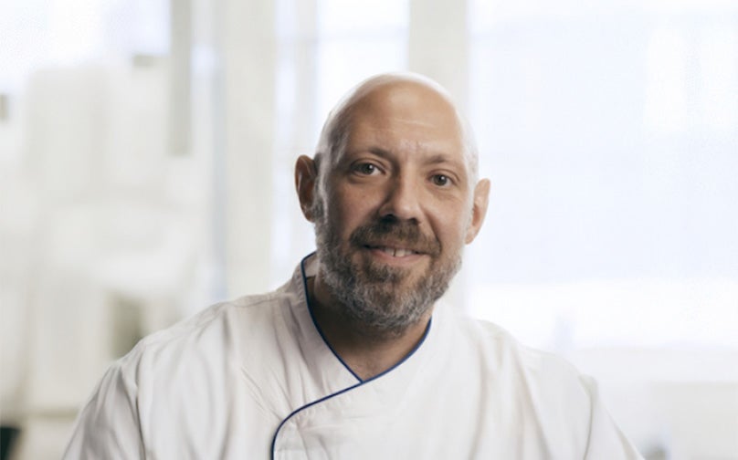 Headshot of Phil Evans wearing a white chef jacket with dark piping in front of a white background.