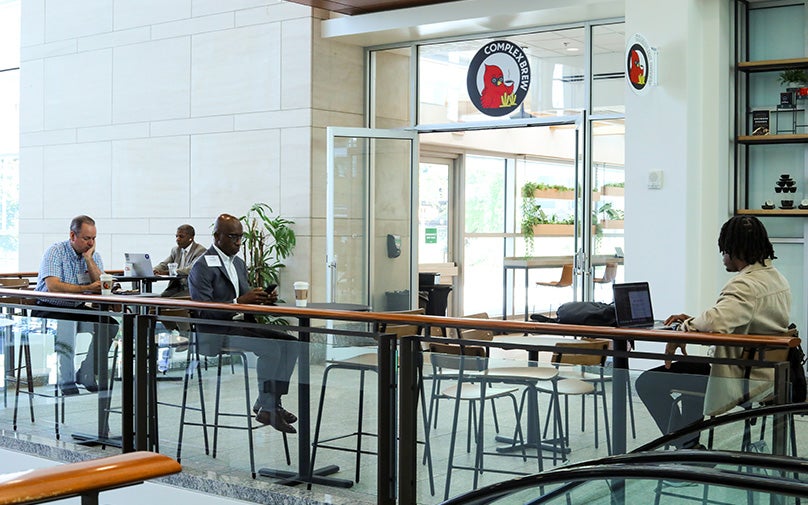 Four individuals pictured working, sitting at their tables in the seating area outside of the coffee shop.