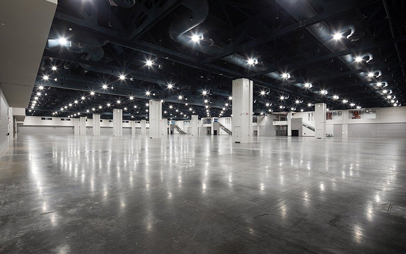 Spacious, empty convention center exhibit hall with high ceilings, bright lighting, and polished floors.