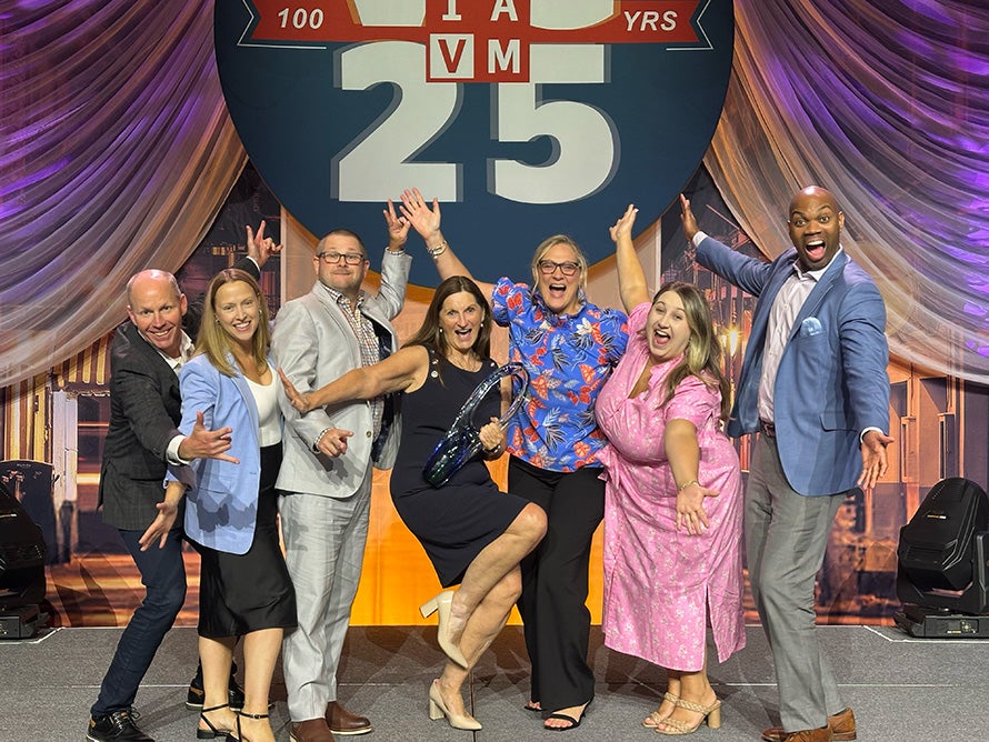 A group of seven people standing with arms outstretched and excited expressions.