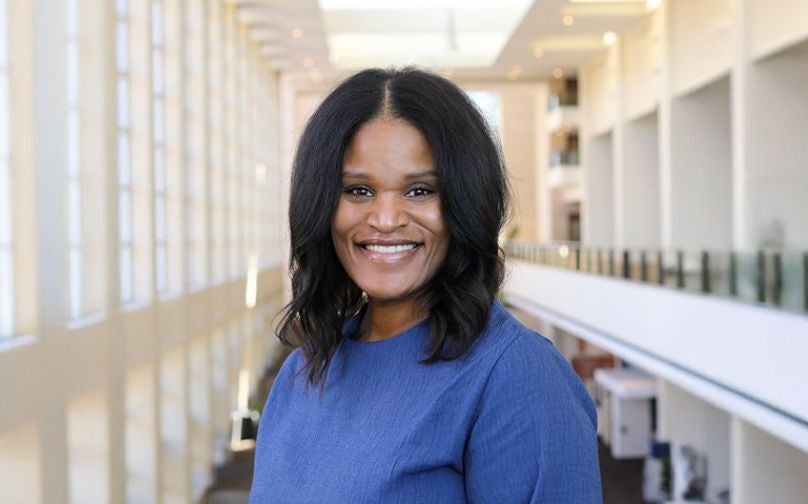 Headshot of Lori Shumpert wearing a blue top standing on an indoor balcony overlooking large windows and the convention center mezzanine.d.
