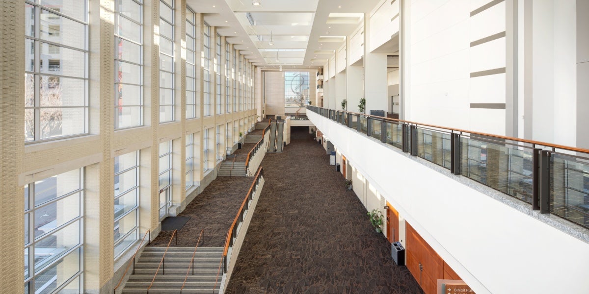 View from above a spacious atrium with floor-to-ceiling windows, modern lighting, neutral tone carpet, and an open mezzanine.