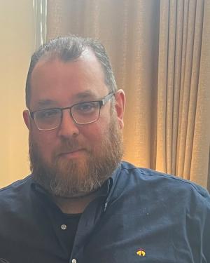 Headshot of Mike Broder wearing glasses and a dark blue button up shirt