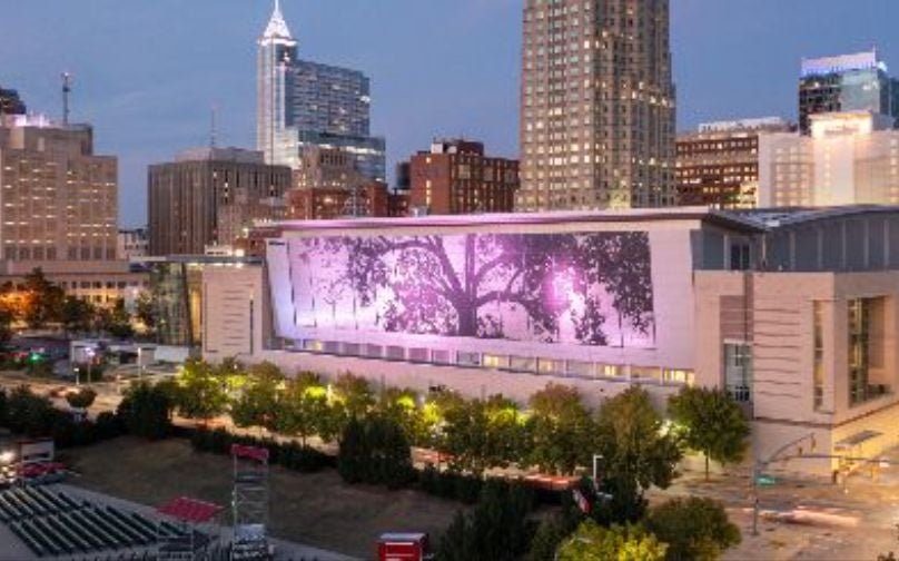 The Downtown Raleigh skyline at dusk, with the convention center and its illuminated shimmer wall featured prominently in the center. 