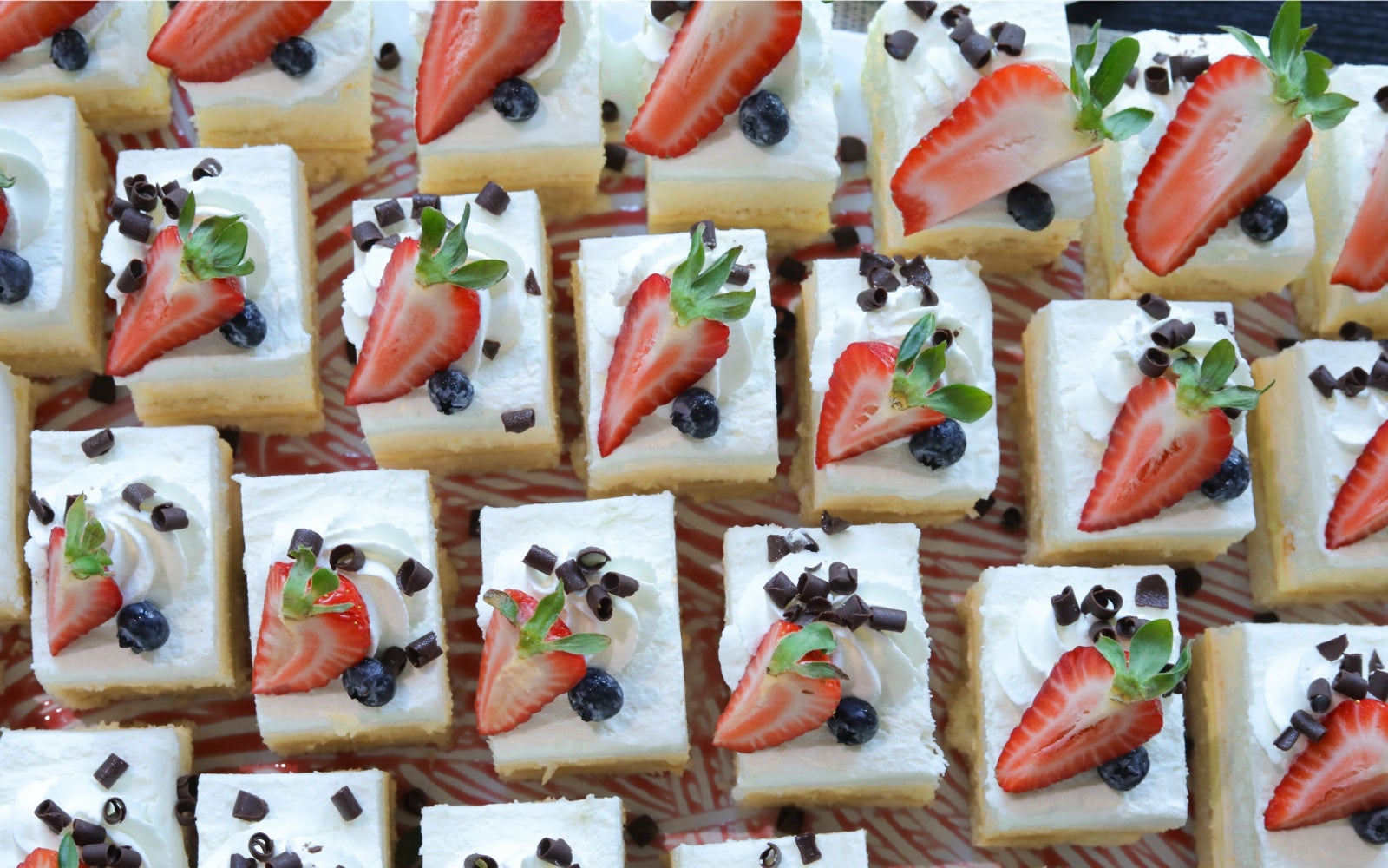 Mini vanilla cakes topped with fresh strawberries, blueberries, whipped cream, and chocolate shavings.