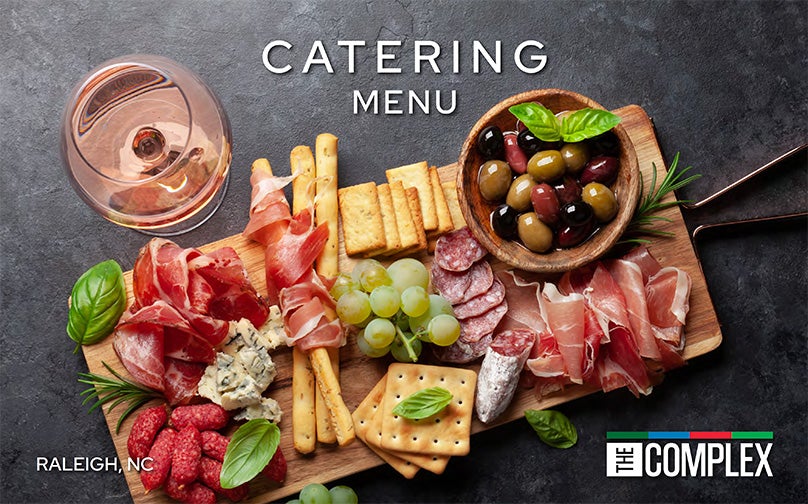 Birds eye view of charcuterie board and wine glass with rose on a charcoal background, the words &quot;Raleigh, NC&quot; in the bottom left corner and The Complex logo on bottom right corner. 