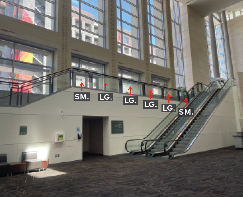 Upper mezzanine landing with railing and glass panels. Next to escalator.