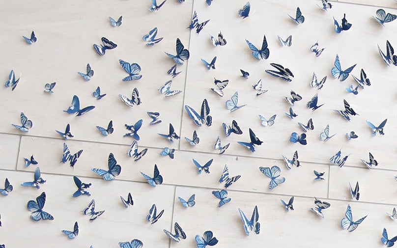 Art installation of 3-D blue butterflies in flight, creating a dynamic and elegant display on a light wall.