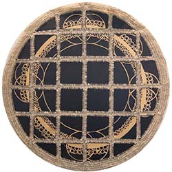 A circular hand-woven tapestry is made of black wooden panels stitched together to create a circle with a beige woven border. A circular design in beige ink shows circles and overlapping circles around the border.