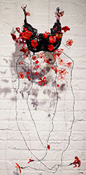 A black bra made from needle lace with red hand-embroidered flowers built around wires hanging down.