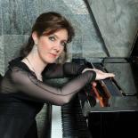 Photo of woman sitting at grand piano looking at camera