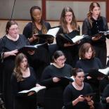 Photo of women in black dresses in choir formation with music folders