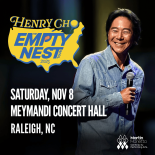 Henry Cho: The Empty Nest Tour promotional artwork Henry Cho standing in blue denim shirt with a mic in hand in front of a black background.