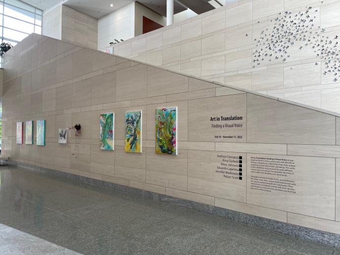 A beige corridor to the South Hallway features the "Art in Translation: Finding a Visual Voice" exhibition. Several works are hung along the corridor, as well as black vinyl descriptions of the exhibit.