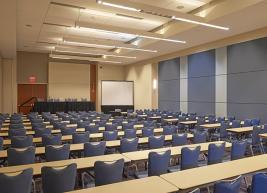 Wide shot of room full of chairs facing a presentation table 