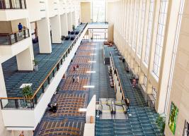 An overhead shot of the RCC's Mezzanine level which shows three levels of the building with green and rust-colored carpeting, beige balconies, and large windows that light up the scene with sunlight.