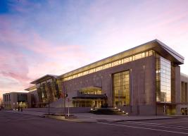 The RCC building at sunrise: a beige building with its many windows illuminated from the inside against a bright blue, purple, and pink sky.