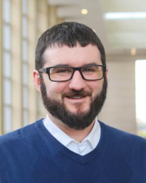 Adult white male with brown short hair and glasses smiles at the camera.