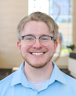Headshot of Liam Aubrey, wearing glasses and blue button up shirt.