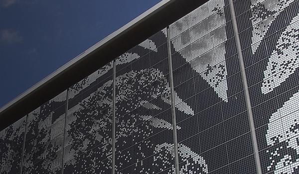 A close-up of the Shimmer Wall against a deep blue sky, showing the thousands of tiles comprising the silver tiled wall which depicts a large black oak tree.