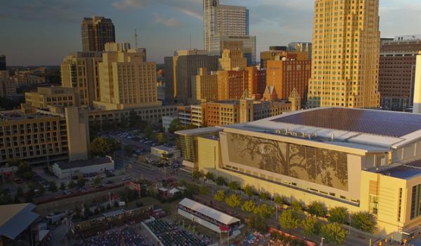 Buildings along the Downtown Raleigh skyline with a focus on the RCC's Shimmer Wall, which is a large silver art installation made up of thousands of tiles displaying the outline of a black oak tree. 